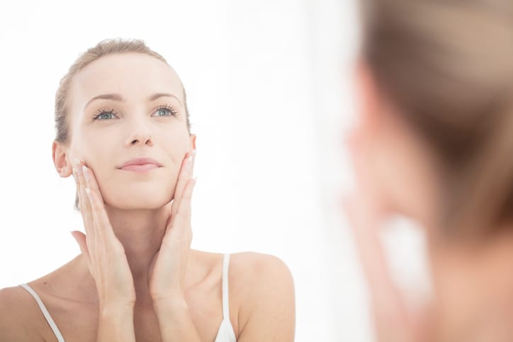 Young woman looking in mirror, applying moisturiser to face